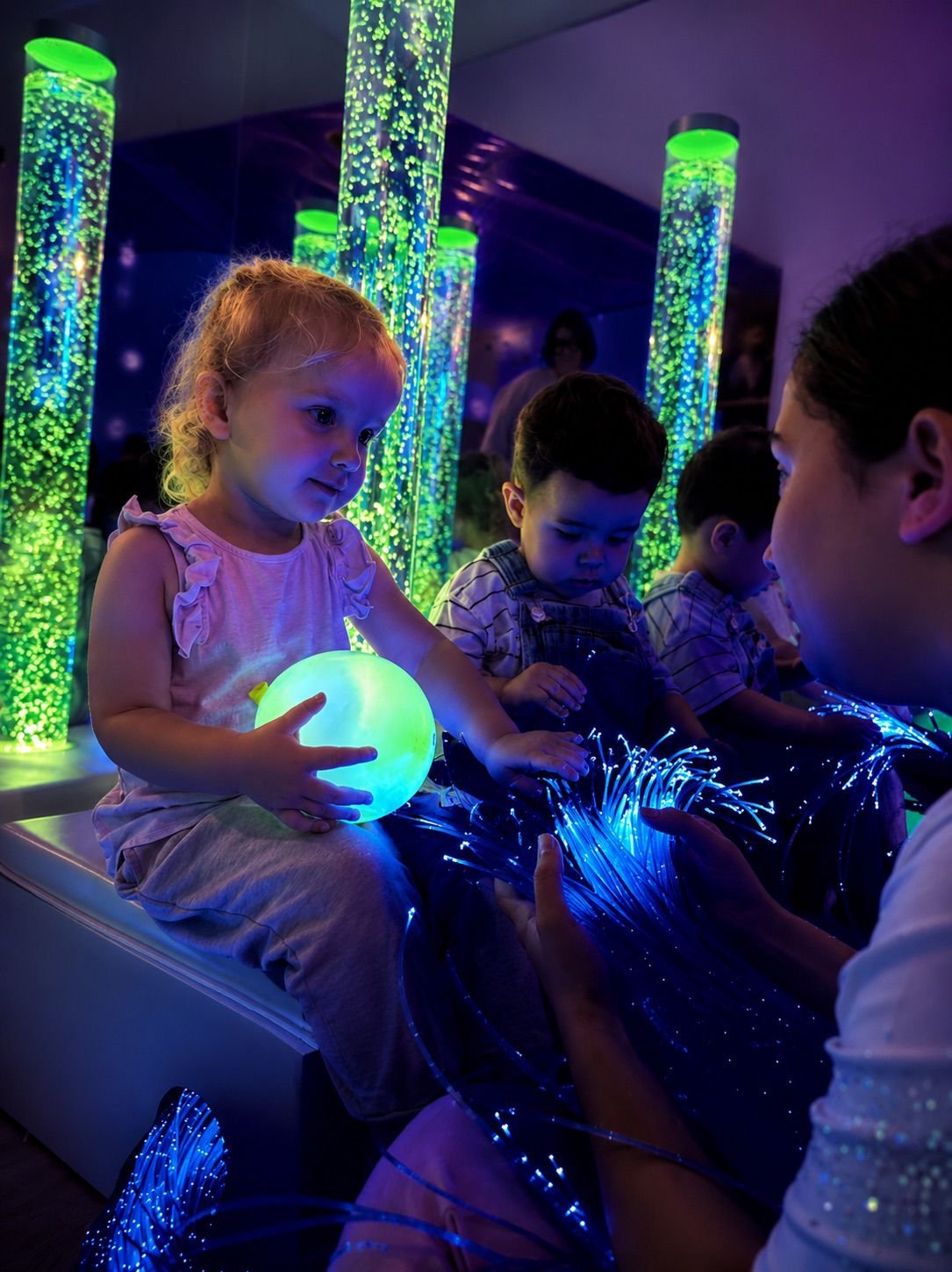 Niños participando en una experiencia sensorial de JACE con columnas de burbujas y fibras ópticas